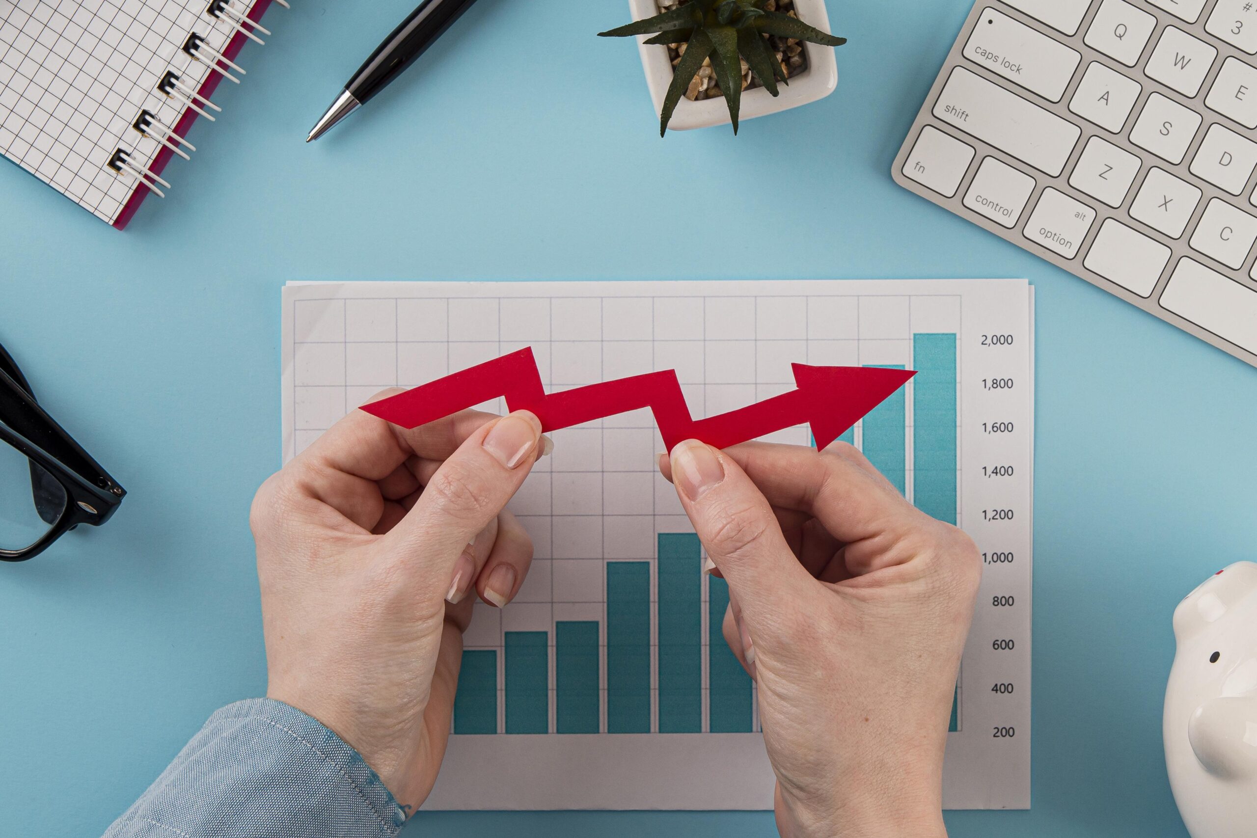 Hands holding a red upward arrow over bar chart, symbolizing business growth and financial resilience, concept for business loans aiding survival during economic downturns.